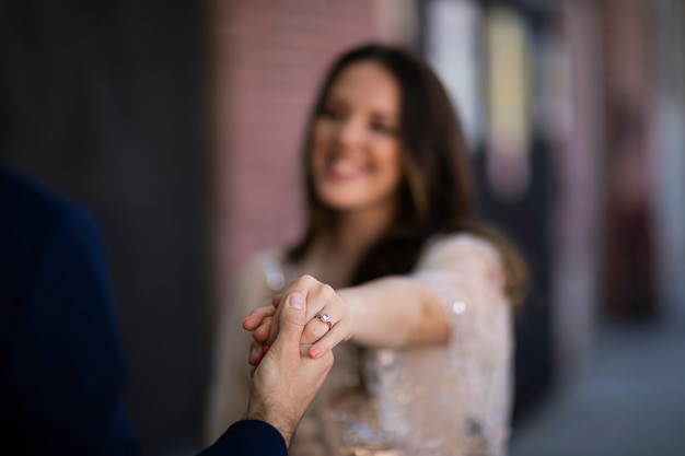 Defokussiertes Paar, das im Freien Händchen hält und Verlobungsring zeigt
