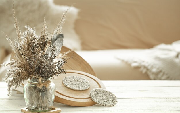 Dekorationsgegenstände im gemütlichen Innenraum des Raumes, eine Vase mit getrockneten Blumen auf hellem Holztisch.