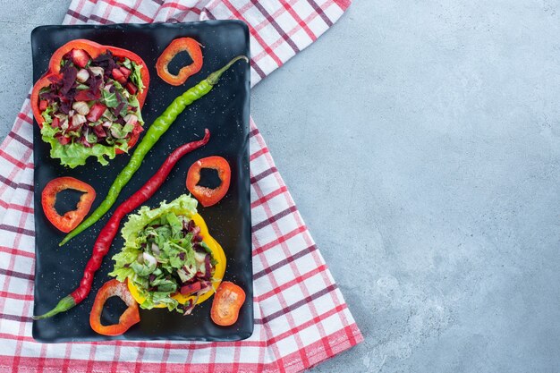 Dekorativ ausgerichtete Portionen Salat auf einer Platte mit geschnittenen Paprika und Chilischoten auf Marmor.