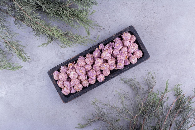 Dekorative immergrüne Zweige und ein Tablett mit bonbonbeschichtetem Popcorn auf Marmorhintergrund. Foto in hoher Qualität