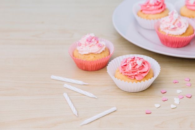 Kostenloses Foto dekorativer kleiner kuchen mit sahne und besprüht auf hölzernem schreibtisch