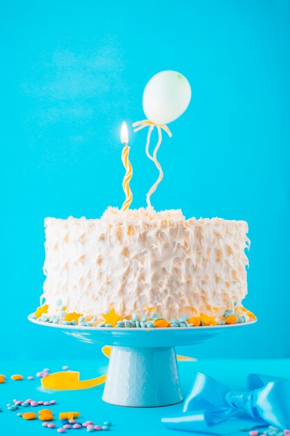 Dekorativer Kuchen mit belichteter Kerze auf blauem Hintergrund