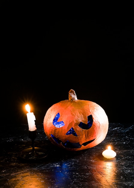 Dekorativer Kürbis Halloweens, der unter brennenden Kerzen auf Seiten liegt