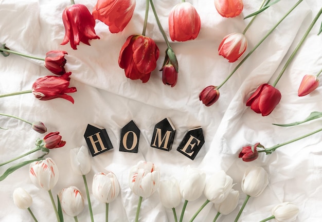 Kostenloses Foto dekoratives wort „zuhause“ und tulpen in einer draufsicht auf ein weißes bett