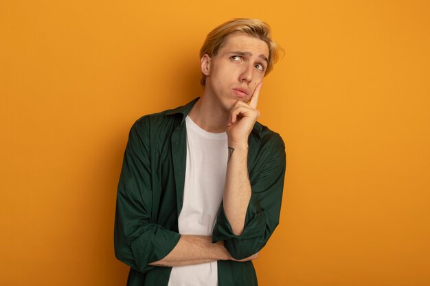 Kostenloses Foto denken, das den jungen blonden kerl der seite betrachtet, der grünes t-shirt trägt, das finger auf wange setzt