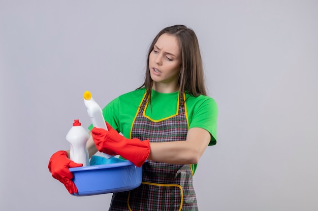 Denken, dass das Reinigen des jungen Mädchens, das Uniform in den roten Handschuhen trägt, Reinigungsmittel auf ihrer Hand auf isolierter weißer Wand betrachtet