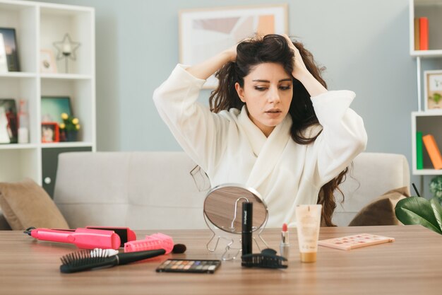 Denken gegriffene Haare mit Blick auf Spiegel junges Mädchen sitzt am Tisch mit Make-up-Tools im Wohnzimmer