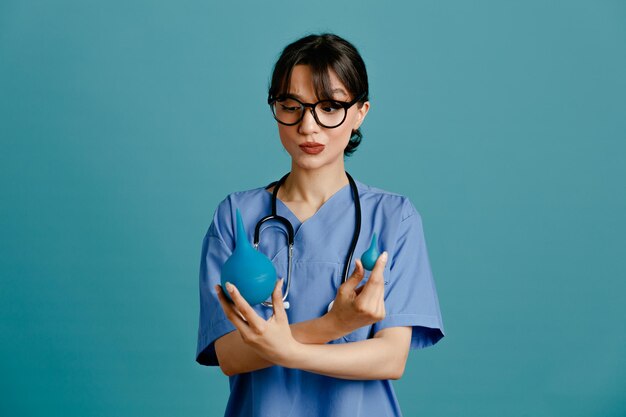Denken, Halten und Überqueren von Einläufen, junge Ärztin, die einheitliches Fith-Stethoskop trägt, isoliert auf blauem Hintergrund