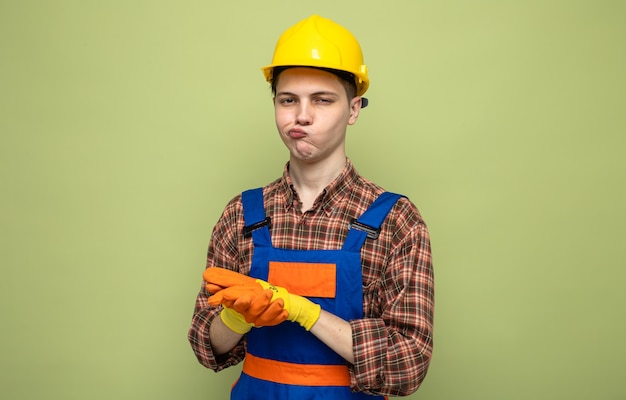 Denken mit den Händen zusammen junger männlicher Baumeister, der Uniform mit Handschuhen trägt