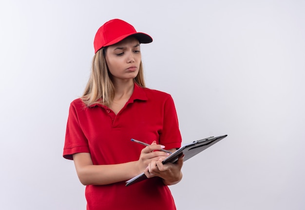 Denkende junge Lieferfrau, die rote Uniform und Kappe trägt, schreiben auf Zwischenablage lokalisiert auf Weiß