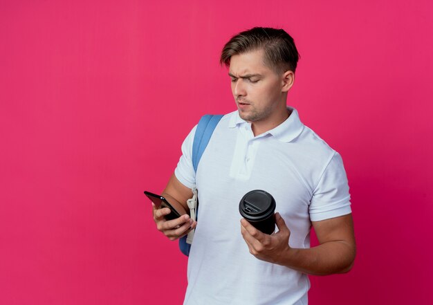 Denkender junger hübscher männlicher Student, der Rückentasche hält, die Tasse Kaffee hält