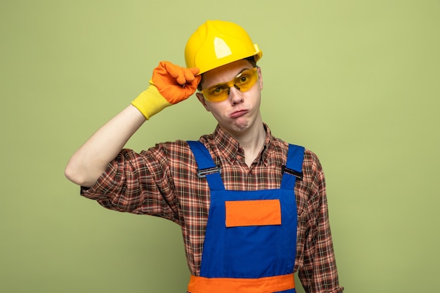 Denkender junger männlicher Baumeister, der Uniform und Handschuhe mit Brille trägt