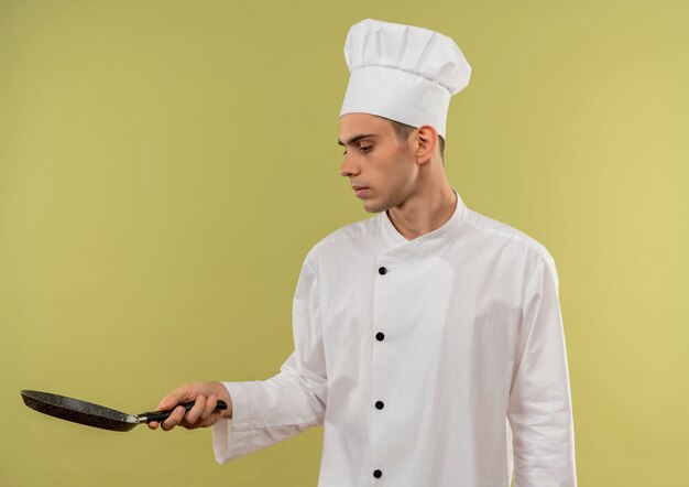 Denkender junger männlicher Koch, der Kochuniform trägt, die Pfanne in seiner Hand mit Kopienraum betrachtet