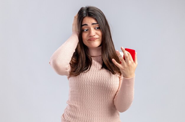 Denkendes junges Mädchen am Valentinstag, das den Ehering hält und betrachtet, der die Hand auf den Kopf legt, isoliert auf weißem Hintergrund