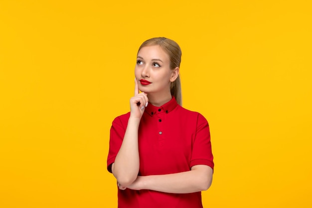 Denkendes Mädchen des roten Hemdtages, das oben in einem roten Hemd auf einem gelben Hintergrund schaut