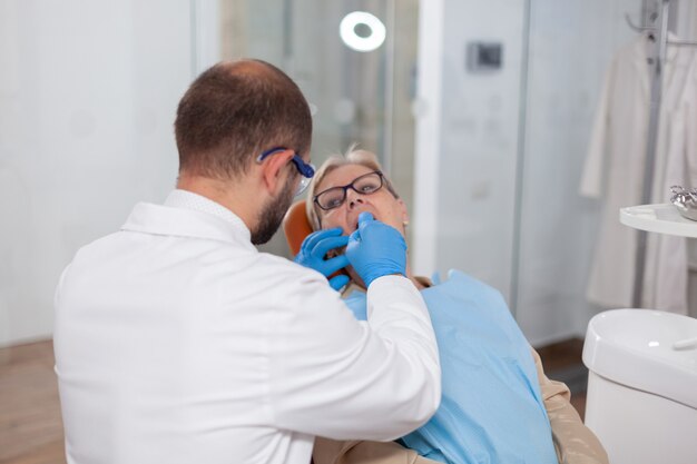 Denstis im schrank, der den zahn des älteren patienten in der zahnklinik repariert. älterer patient während der ärztlichen untersuchung beim zahnarzt in der zahnarztpraxis mit orangefarbener ausrüstung.