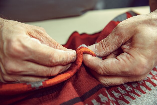 Der ältere Mann, der in seiner Schneiderei arbeitet, schneidet, hautnah. Textil Vintage Industrie. Der Mann im Frauenberuf. Konzept der Gleichstellung der Geschlechter