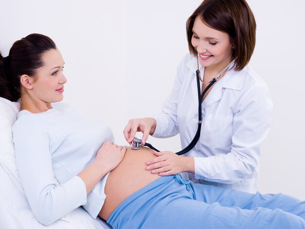 Der Arzt hört den Bauch einer schwangeren Frau