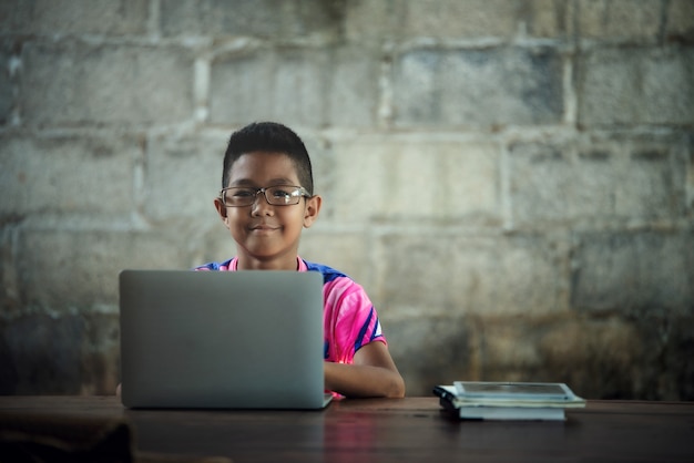 Der asiatische Junge, der auf dem Tisch Laptop verwendet, kommen zu shcool zurück