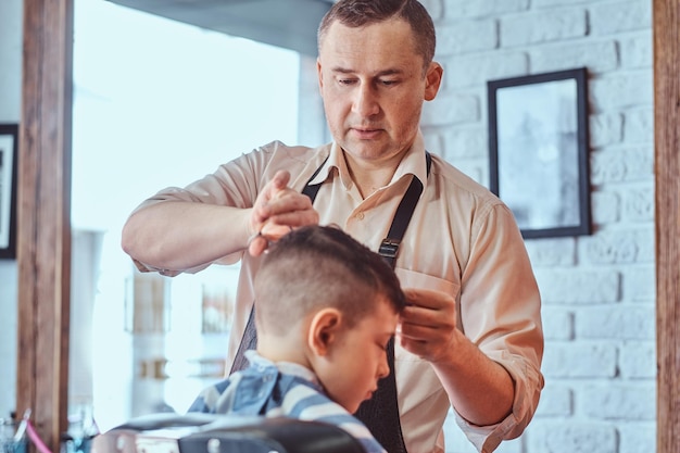 Der attraktive schuljunge bekommt einen trendigen haarschnitt von einem reifen friseur im modischen friseursalon.