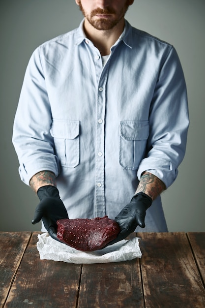 Der bärtige Hipster-Metzger in schwarzen Handschuhen bietet ein Stück Walfleischsteak an