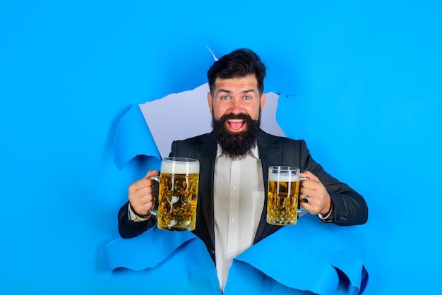 Der bärtige mann mit lager und dunklem bier hält craft-bier, der durch ein papierloch schaut, stilvoller mann, der trinkt