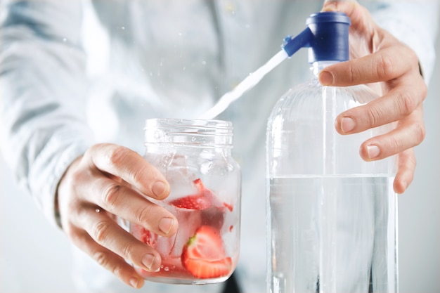 Der Barkeeper mit engem Fokus macht hausgemachte Limonade, gießt Mineralwasser in ein rustikales Glas mit Erdbeerscheiben und Eiswürfeln