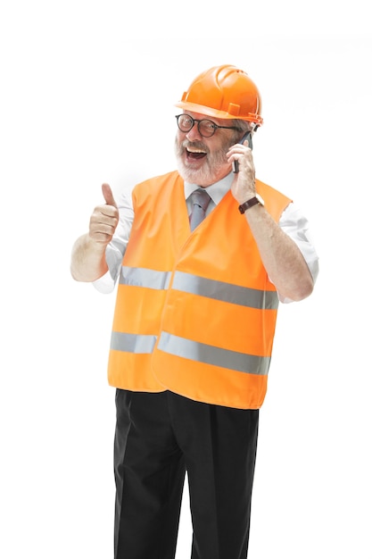 Der Baumeister in einer Bauweste und einem orangefarbenen Helm spricht auf einem Handy über etwas