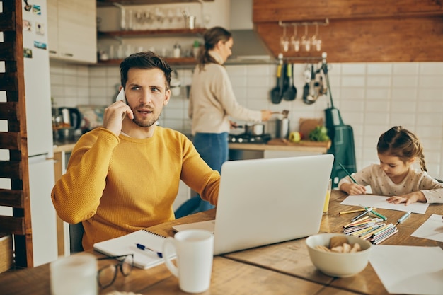 Der berufstätige Vater telefoniert, während er zu Hause einen Laptop benutzt