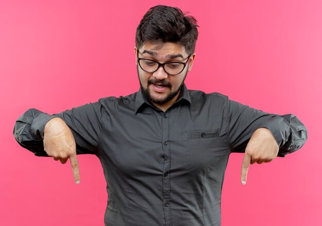 Der Blick auf den beeindruckten jungen Geschäftsmann, der eine Brille trägt, zeigt auf die auf der rosa Wand isolierte Daune