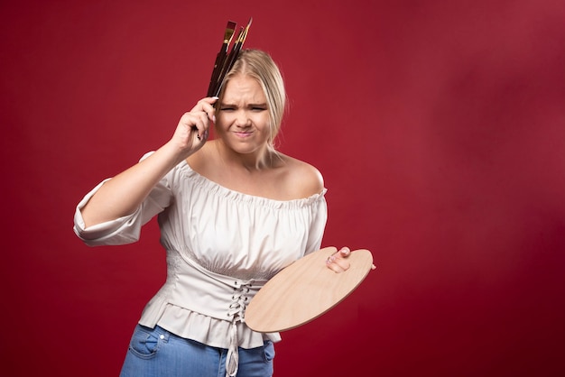 Der blonde Künstler hält eine Palette und Pinsel und sieht überrascht und verwirrt aus.