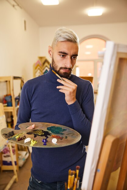 Der blonde Mann zeichnet ein Gemälde mit Öl