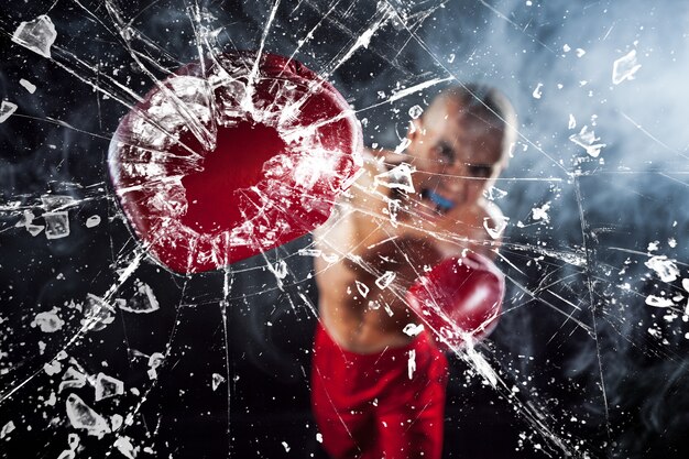 Der Boxer zerquetscht ein Glas. Der junge männliche Athlet kickboxen auf einem blauen Rauch