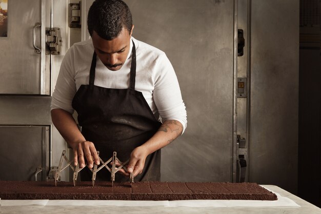 Der Chef des schwarzen Mannes verwendet einen professionellen Vintage-Separator, um den Schokoladenkuchen vor dem Verpacken zu gleichen Teilen aufzuteilen