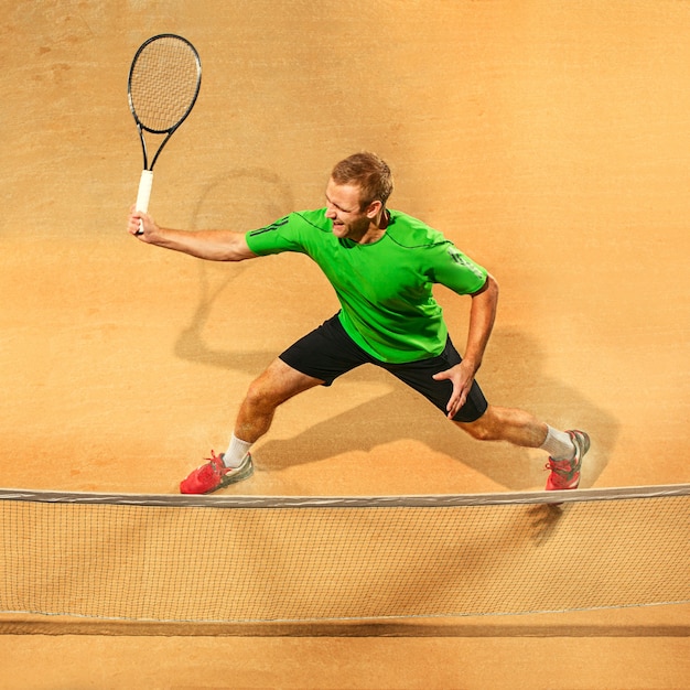 Der eine springende Spieler, kaukasischer fitter Mann, der Tennis auf dem irdenen Platz spielt