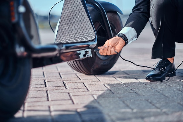 Kostenloses Foto der elegante mann lädt seinen elektroroller mit ladegerät auf einem speziellen parkplatz auf.