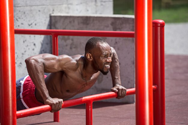 Der fitte Athlet macht Übungen im Stadion. Afro oder Afroamerikanermann im Freien an der Stadt. Sportübungen hochziehen. Fitness-, Gesundheits-, Lifestyle-Konzept