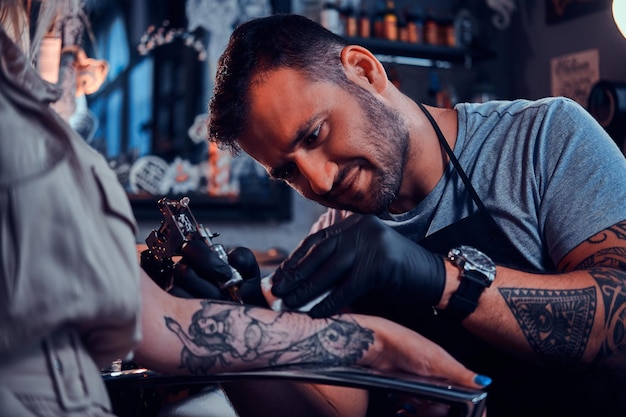 Der fleißige, fokussierte Tätowierer kreiert im Tattoo-Studio ein neues Tattoo auf der Hand einer jungen Frau.