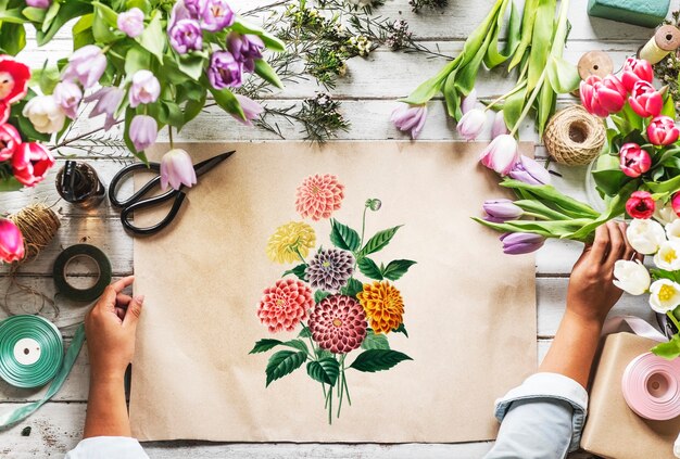 Der Florist, der leeres Design-Raum-Papier auf Holztisch mit frischen Blumen zeigt, verzieren