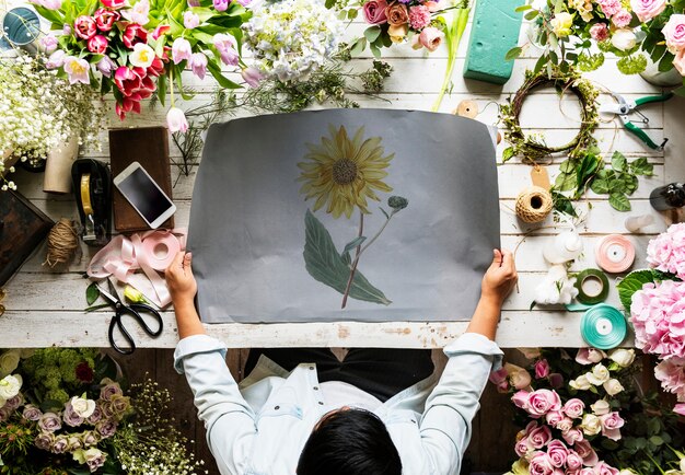 Der Florist, der leeres Design-Raum-Papier auf Holztisch mit frischen Blumen zeigt, verzieren