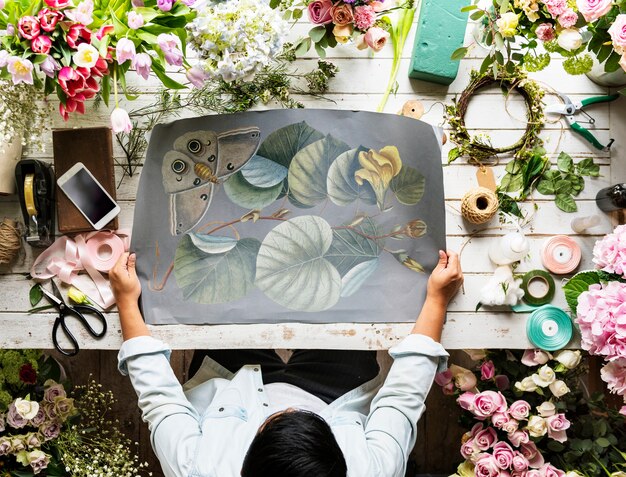 Der Florist, der leeres Design-Raum-Papier auf Holztisch mit frischen Blumen zeigt, verzieren