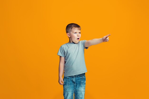 Der glückliche jugendlich Junge, der auf Sie zeigt, halbes Länge Nahaufnahmeporträt auf orange Hintergrund.