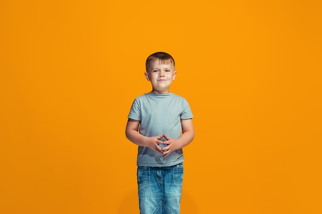 Der glückliche jugendlich Junge, der gegen orange Raum steht und lächelt.