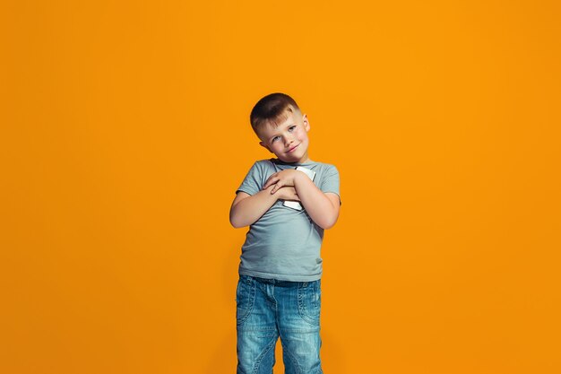 Der glückliche jugendlich Junge, der gegen Orange steht und lächelt.