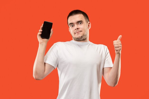 Der glückliche Mann, der am leeren Bildschirm des Handys gegen orange Hintergrund zeigt.