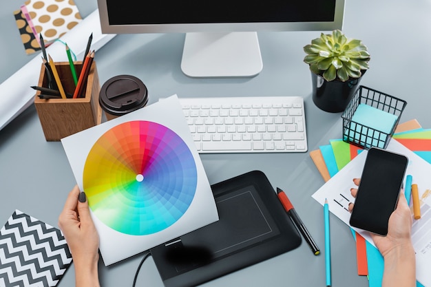 Der graue Schreibtisch mit Laptop, Notizblock mit leerem Blatt, Blumentopf, Stift und Tablette zum Retuschieren