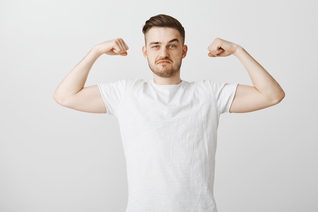 Der hübsche junge Mann zeigt seine Stärke, spannt die Muskeln und lächelt stolz