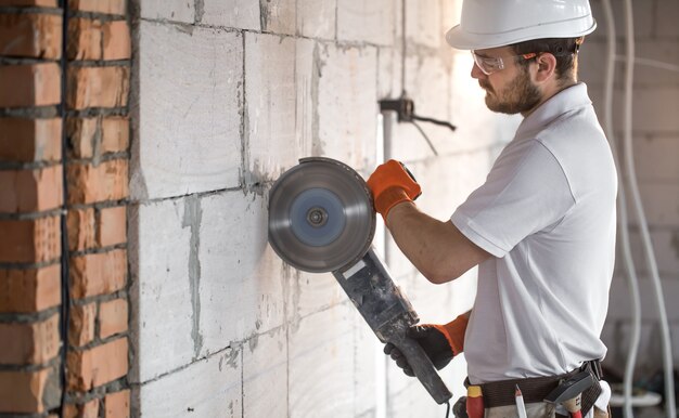 Der Industriebauer arbeitet mit einem professionellen Winkelschleifer, um Ziegel zu schneiden und Innenwände zu bauen. Elektriker.