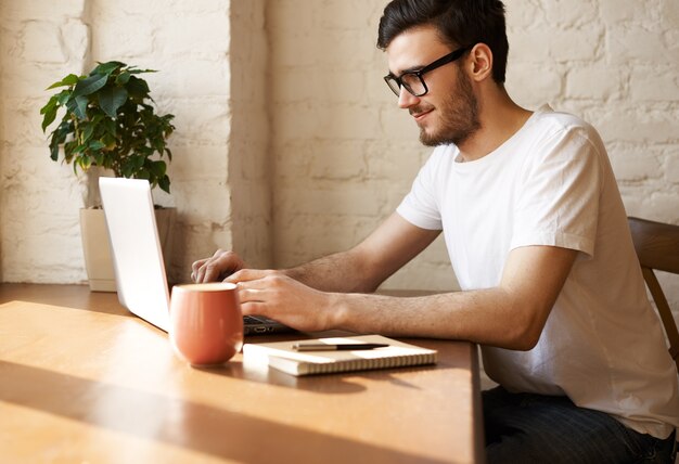 Der junge bärtige Journalist mit Brille schreibt einen neuen Artikel im Internet und beantwortet Fragen seiner Leser