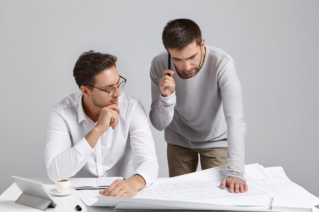 Der junge, erfahrene Architekt trägt ein formelles Hemd und eine Brille und unterrichtet seinen männlichen Schüler oder Auszubildenden